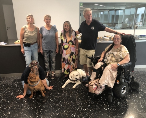 Photo de groupe joyeuse avec des membres et chiens d’assistance posant devant un comptoir décoré pour les 20 ans de l'Association L'Autre Regard.