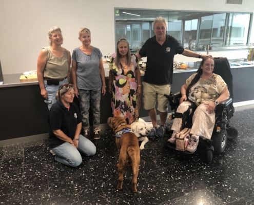 Photo de groupe joyeuse avec des membres et chiens d’assistance posant devant un comptoir décoré pour les 20 ans de l'Association L'Autre Regard.