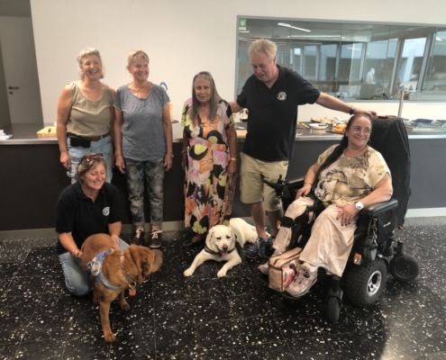 Photo de groupe joyeuse avec des membres et chiens d’assistance posant devant un comptoir décoré pour les 20 ans de l'Association L'Autre Regard.