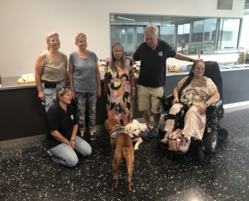 Photo de groupe joyeuse avec des membres et chiens d’assistance posant devant un comptoir décoré pour les 20 ans de l'Association L'Autre Regard.