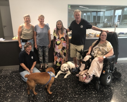 Photo de groupe joyeuse avec des membres et chiens d’assistance posant devant un comptoir décoré pour les 20 ans de l'Association L'Autre Regard.