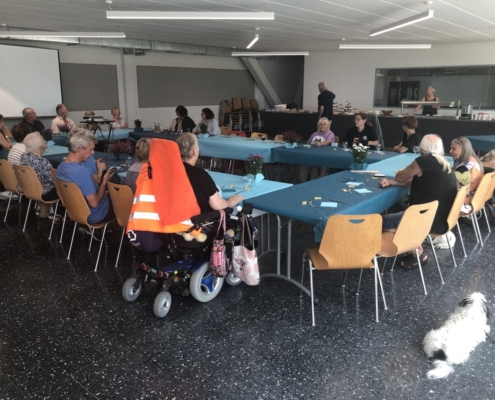 Invités assis autour d'une table, discutant dans une salle lumineuse lors des 20 ans de L'Association L'Autre Regard.