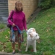 Une dame âgée tenant son chien d’assistance Nino, debout sur une pelouse près d’un bâtiment en briques.