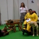 Une dame en fauteuil avec son chien d’assistance, un autre chien tirant une charrette, et une dame en arrière-plan qui l'observe.